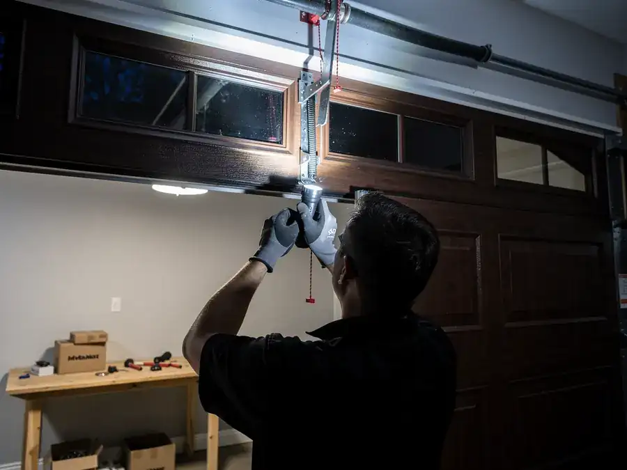 A technician works on a garage door opener with a flashlight.