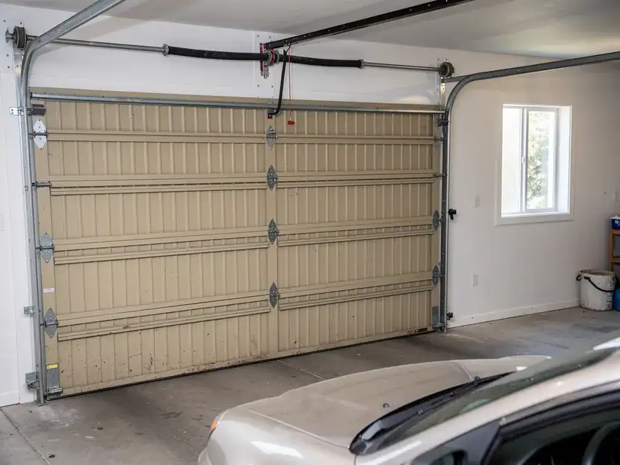 A beige garage door is closed with a car parked in front of it.